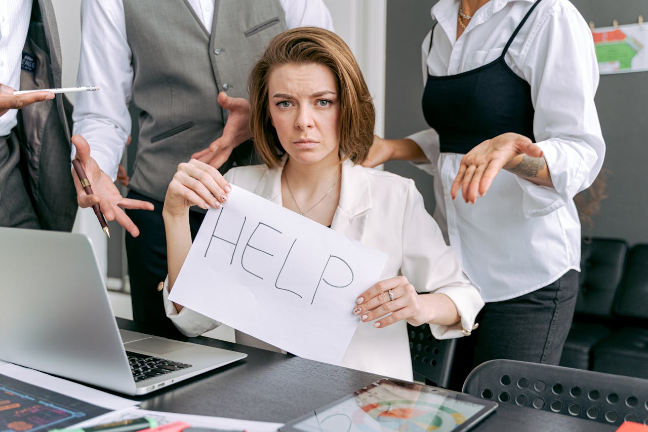 Stressed office worker holding a help sign surrounded by colleagues demands.